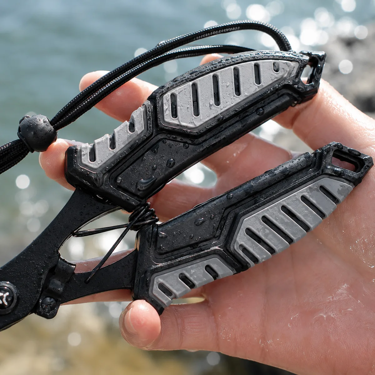 Wet HookGrip pliers held in a wet hand at the water's edge, water beaded across the textured grey and black handle panels